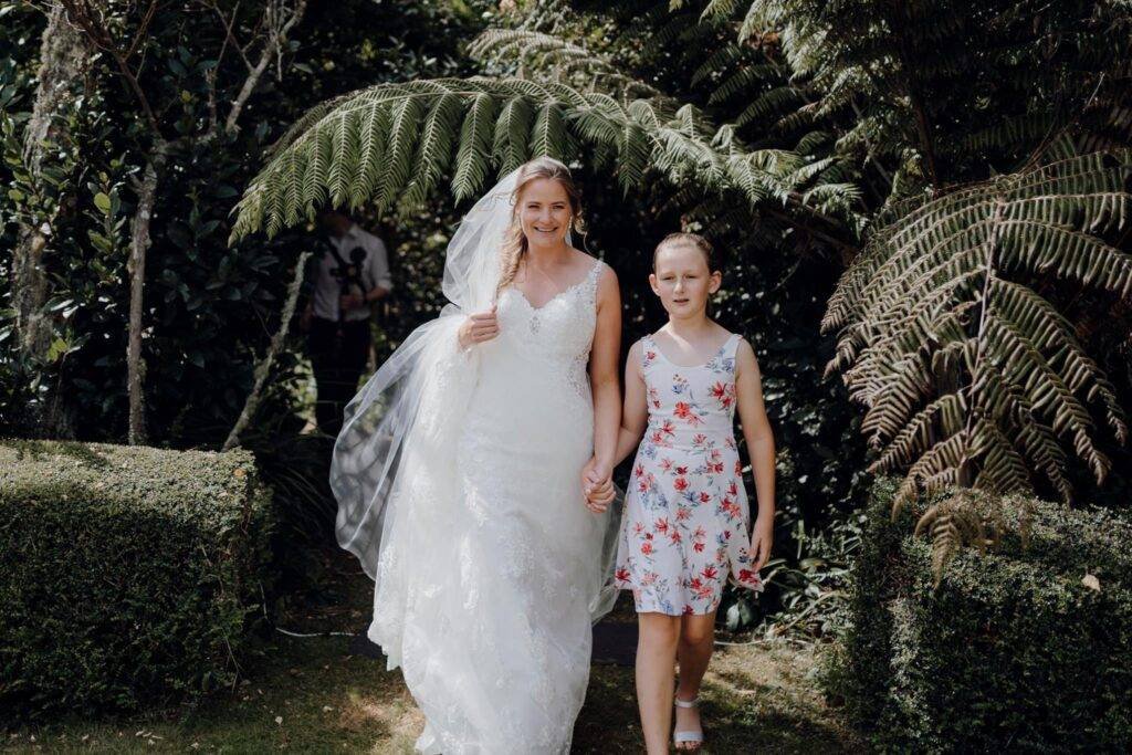 Mother and Daughter Walk Up The Aisle Holding Hands Shaded By Ferns